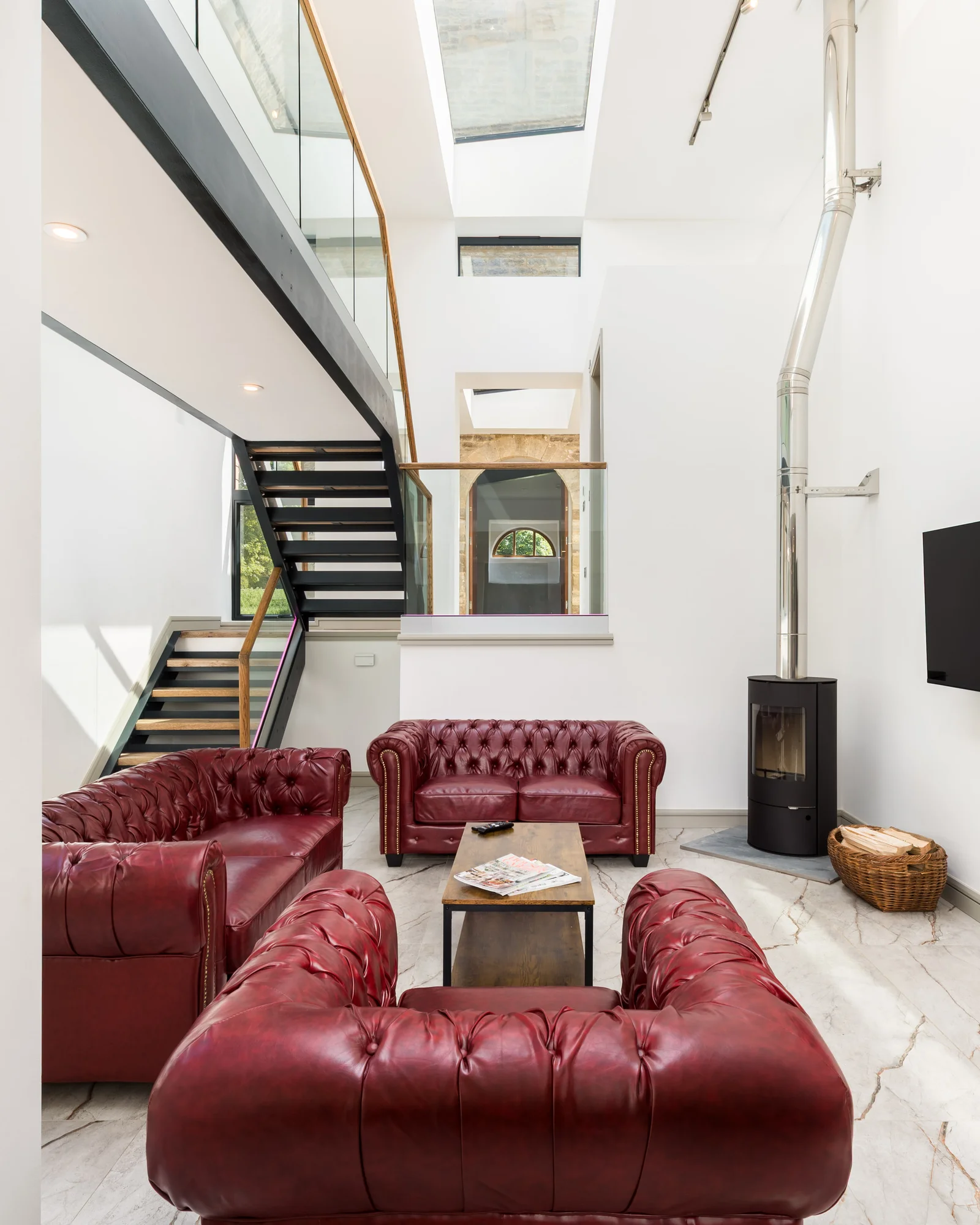 Double height sitting room with oxblood leather chesterfields beneath a glazed stairwell