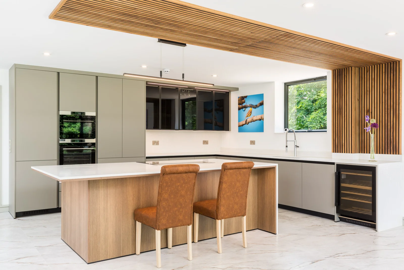 Kitchen island with oak framed chairs on a pale marble effect floor