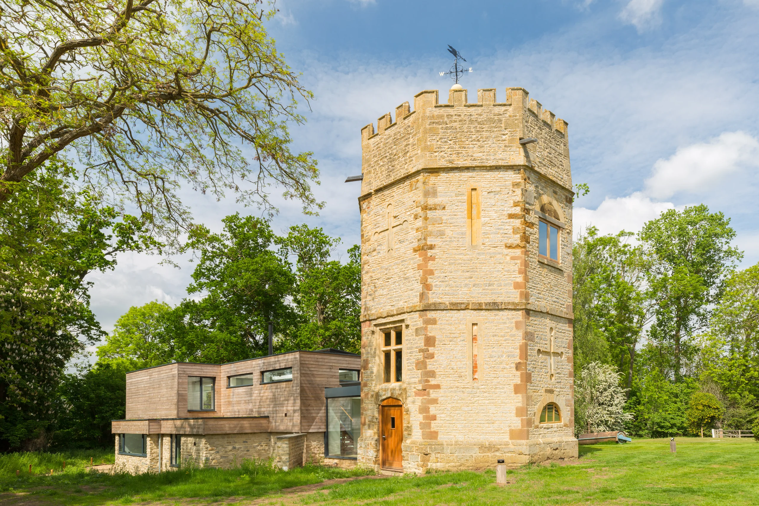 Crenellated stone folly tower beside its contemporary timber and stone extension